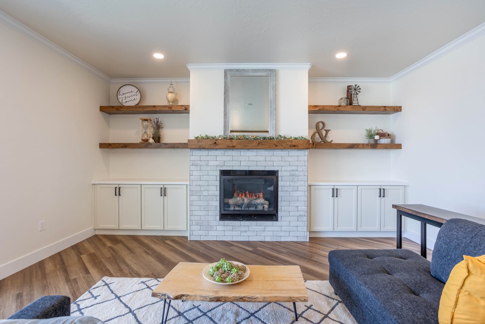 Living room with white brick fireplace, floating wood shelves and built-ins